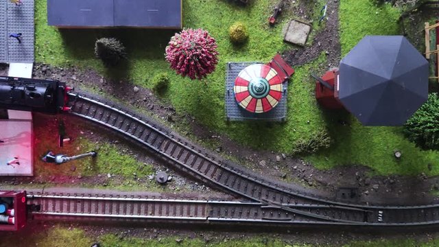 Top view of a moving model of a steam locomotive. Detailed model of peron and train station. Thumbnail close-up