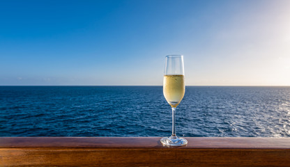 One single glass of sparkling white wine on wooden railing of cruise ship. Sea in the background. Clear blue sky. Alcoholic drink on summer vacation.