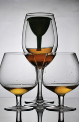 Wine glass goblets on short legs. Nearby are glasses on a long leg. In one of them a funnel is installed. There is a small amount of alcohol in the glasses.