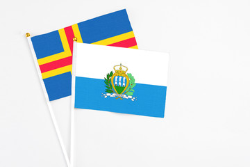 San Marino and Aland Islands stick flags on white background. High quality fabric, miniature national flag. Peaceful global concept.White floor for copy space.