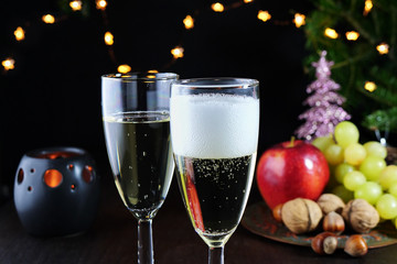 Sparkling white wine in two glasses on Christmas table. Christams tree, lights and decorations in the background
