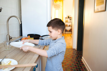 little boy washing dishes in domestic kitchen. Child helping his parents with housework
