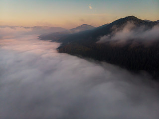 Scenic landscape with fog in mountains. Foggy river in valley illuminated with rising sun. Aerial drone view.