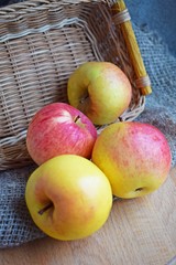 Beautiful ripe apples in a wicker basket on a wooden background.