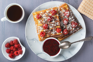 Homemade waffles with raspberries and jam in a plate on a gray table