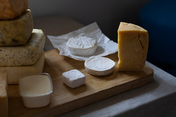 Cheese wheels produce for sale on the counter. Fresh cheese loaf selection, pile of many cheese mix. Beautiful light from the window.