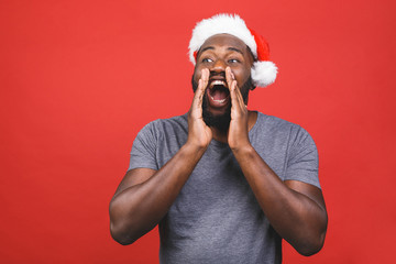 New year and black friday sale! Happy screaming black african american man in christmas hat isolated on red background.
