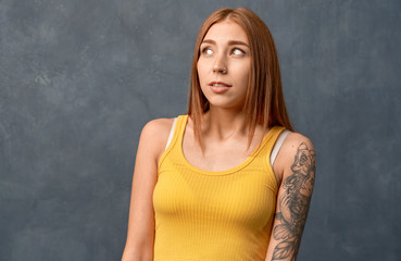 Surprised scared woman astonishing, gasps from fear. Beautiful girl ginger long hair and tattoo on arm, wearing yellow top, isolated on wall in Studio with free space for your advertisement 