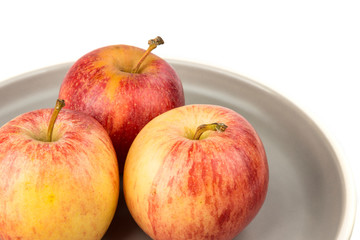 Plate of three whole ripe raw yellow and red apples
