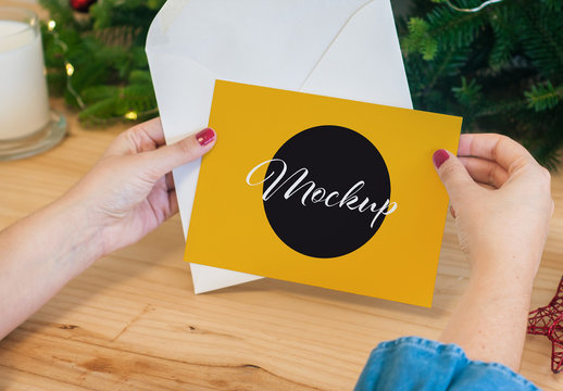 Hands Holding a Postcard with Envelope and Christmas Decoration Mockup