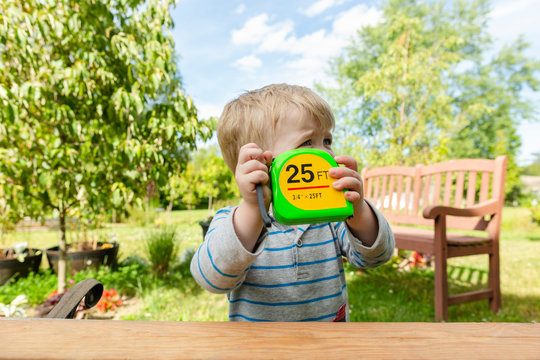 Small boy holds up measuring tape while outdoors measuring in backyard