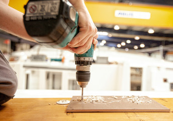 Close up of man drilling wood with a drill machine in a workshop