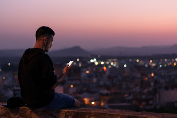 Man is looking his smartphone at night, lights of the city are on background
