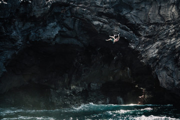 man climbing above the ocean in a volcanic cave