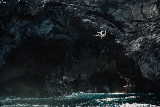 man climbing above the ocean in a volcanic cave