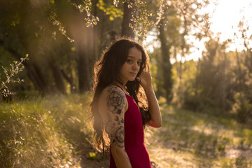 Portrait of a young girl in a red dress in a forest at sunset. Fantasy vibes