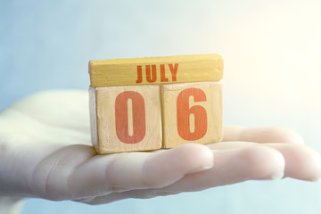 july 6th. Day 6 of month,Handmade wood cube with date month and day on female palm summer month, day of the year concept