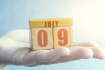 july 9th. Day 9 of month,Handmade wood cube with date month and day on female palm summer month, day of the year concept