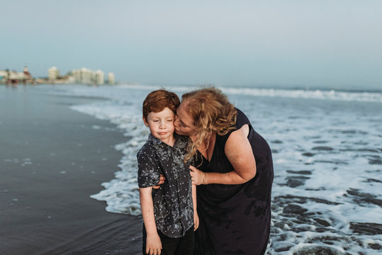 Son making funny face while mother kisses him at dusk at the beach