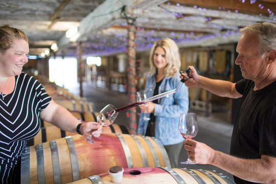 Winemaker pours wine sample using a pipette in storehouse.