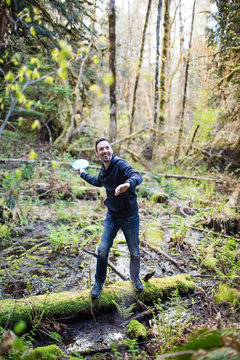 Man throws frisbee in forest while balancing on fallen tree.