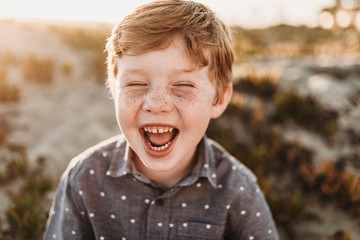 Front view of young kindergarten age boy laughing during beach sunset