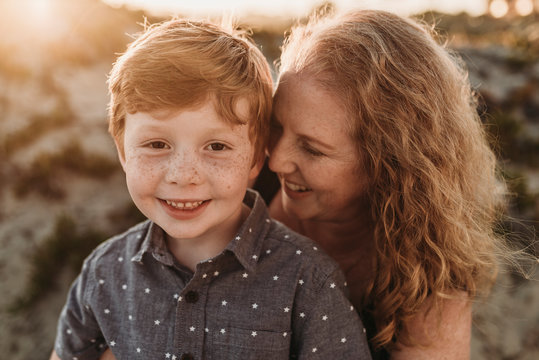 Front view of mother hugging redheaded kindergarten age son at sunset