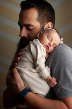 Newborn baby girl sleeping on father's shoulder at home in soft light