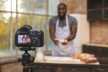 Baking process. Young cooking african man speaker talking on digital camera recording vlog. African...