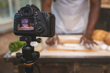 Baking process. Young cooking african man speaker talking on digital camera recording vlog. African...