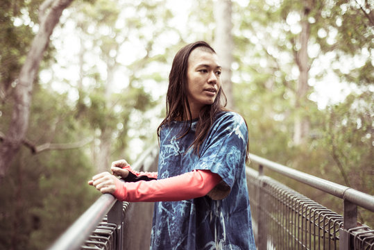 androgynous asian with ninja shave looks at forrest on tree top walk