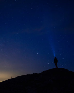 A man stares up at the night sky with a headlamp.