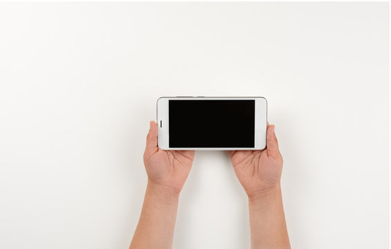 The little girl is holding a horizontally positioned mobile phone. Modern gadgets in the hands of small children. Top view close-up on a smartphone in the hands of a child.