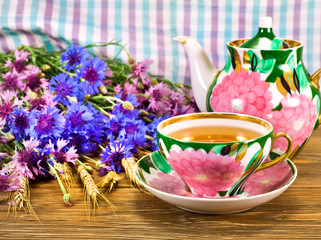 Black tea in a cup with painted teapot, blue cornflowers and wheat ears on a wooden background.