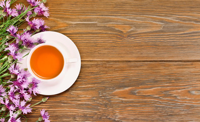 Black tea in cup with pink cornflowers on a wooden background. Top view. Copy space.