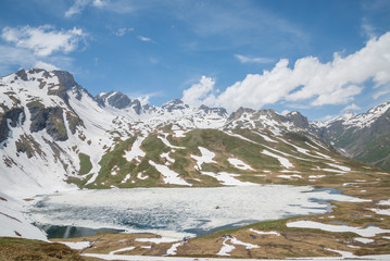 Verney lake, Italian Alps, La Thuile. Ice and snow are melting, the lake and grass on the hills begins to show