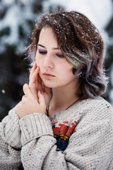 A girl of Caucasian appearance in a sweater and jeans on a background of snowy trees. Snowy winter...