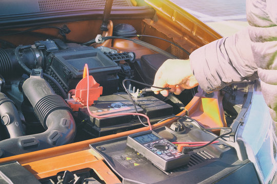 Measurement of battery voltage in a car. Driver inspection holding battery capacity tester voltmeter. Toned image.