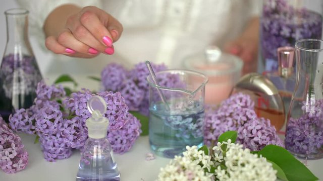 Making body care production beauty aroma bottle of perfume lilac flowers background, Hand of female perfumer lab technician chemist cosmetician pouring cosmetic aroma glass test tube oil in liquid 4 K