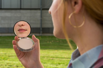 Young woman with nose piercing looking at beauty mirror in her hand