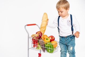 cheerful little boy in casual clothes standing in studio with healthy food basket. Shopping, discount, sale concept
