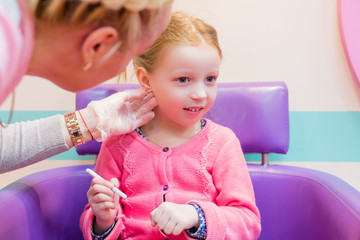 cute little girl having ear piercing process with special equipment in beauty center by medical worker. piercing the ears of a girl in a beauty salon, in a Barber shop