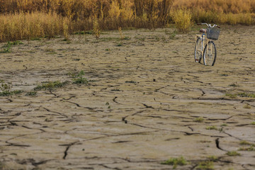 Yellow bike on colorful dry soil surface with deep black cracks
