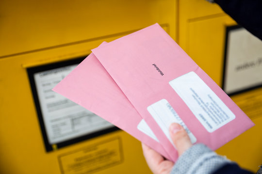 Elector holding documtents for the postal vote in front of the mailbox