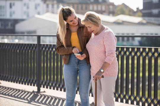 Granddaughter and her grandmother walking on footbridge and using smartphone