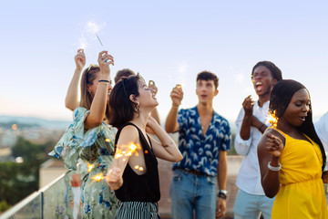 Group of happy multi-ethnic friends celebrating a party in the evening, holding sparklers