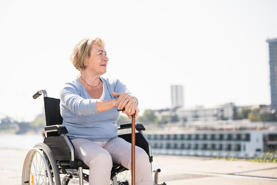 Senior woman sitting in wheelchair, with walking stick