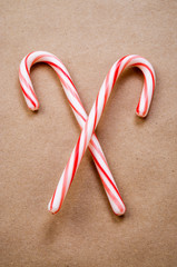 Pair of Christmas candy canes criss-crossed on simple brown paper background 