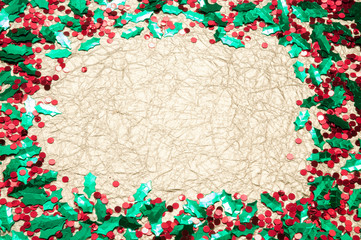 Holiday frame of sprinkles of shiny green and red holly and berries confetti with neutral gold copy space