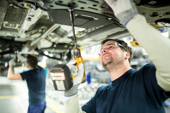 Two colleagues working at car underbody in modern factory